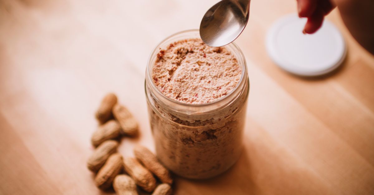 Pot de beurre de cacahuète maison avec une cuillère et des cacahuètes sur une table en bois